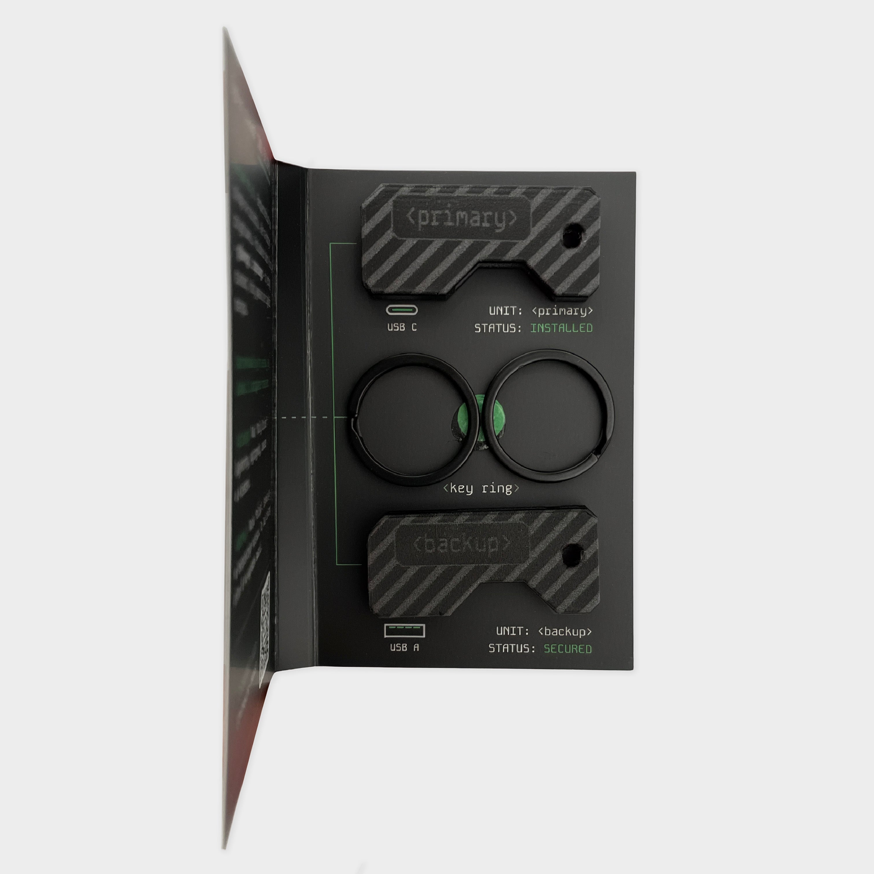 Prezent dla Informatyka_Etui Lock Nest Pivot do kluczy sprzętowych Yubikey Opakowanie Czarny zestaw dwóch ochronnych etui na klucze YubiKey z grawerem „primary” oraz „backup”. Widoczny klucz YubiKey 5C NFC oraz YubiKey 5 NFC w wersji USB-A wysunięte z obudów. Idealne rozwiązanie do odróżnienia klucza głównego od zapasowego. 